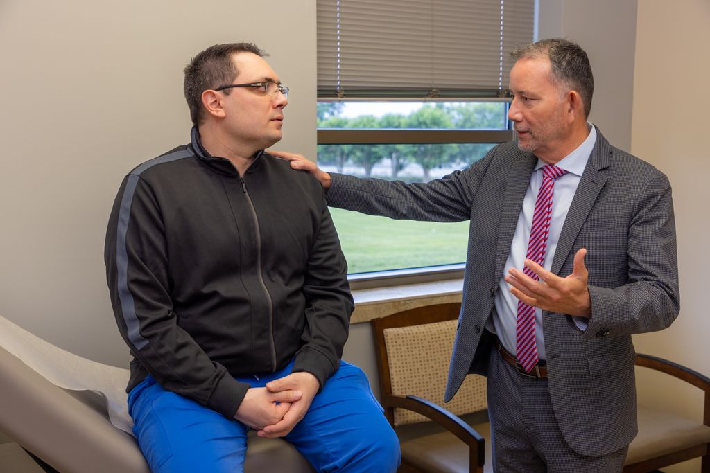 Physician in a suit consulting with a seated patient in an exam room at Gadsden Cancer Clinic