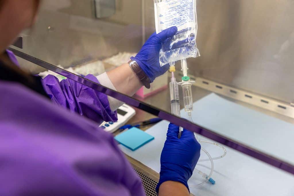 Gowned and gloved staff member preparing an IV chemotherapy bag inside a biosafety cabinet at Gadsden Cancer Clinic.